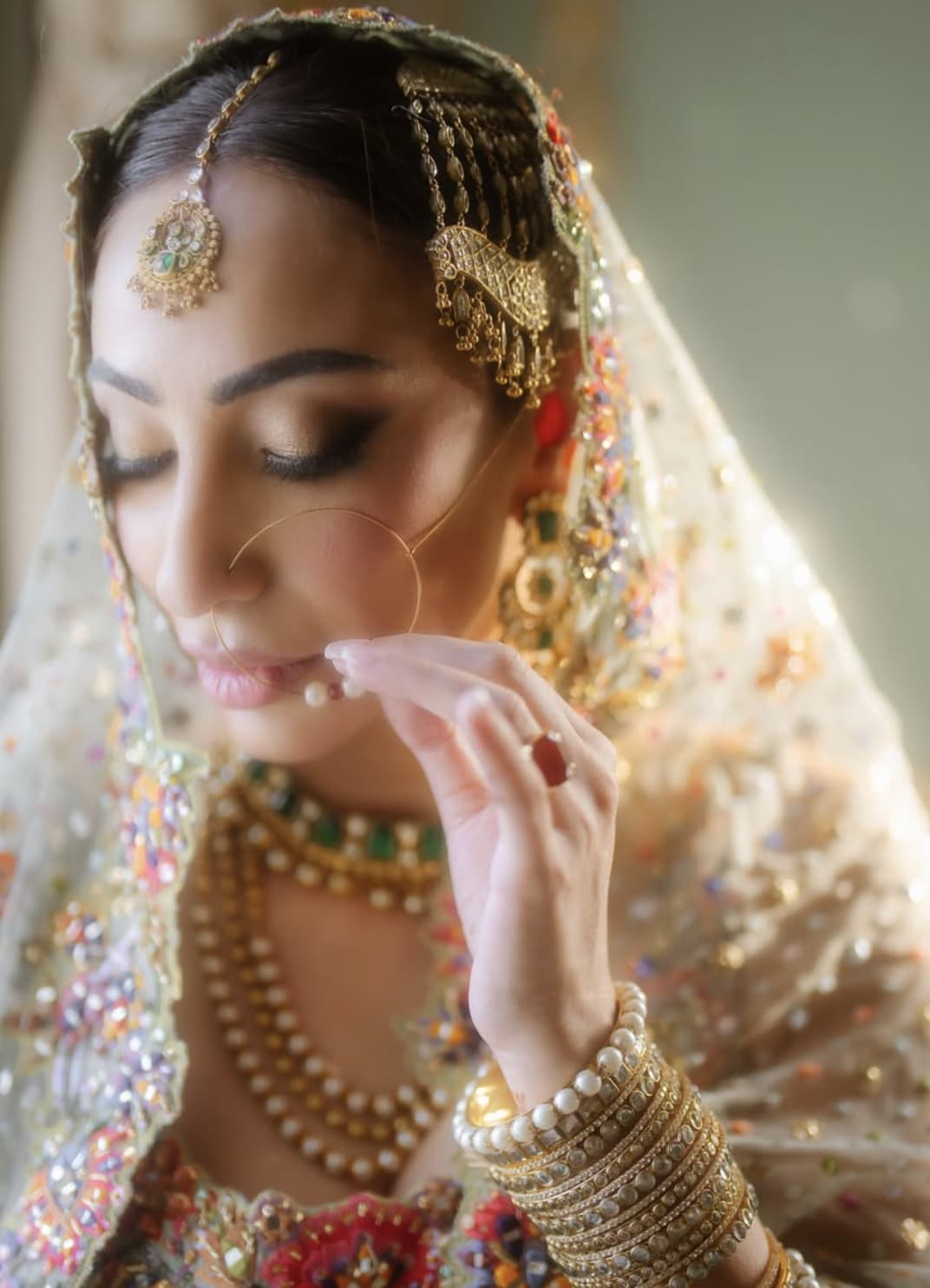 A bride's hand lifts to her nath, pearls at her throat