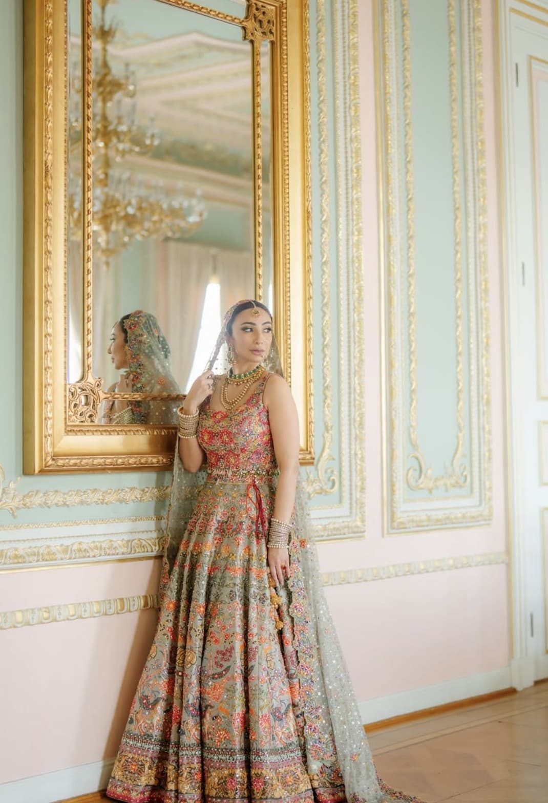 A bride beside a gilded mirror in a pale green room