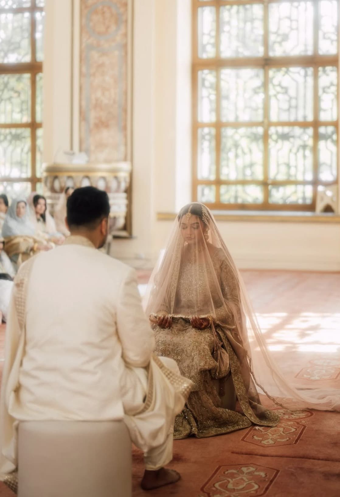 A bride sits with bowed head beneath her veil as the nikah is read